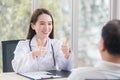 Asian professional woman doctor smiles and shows thump up sign or Ã¢â¬ÅVery goodÃ¢â¬Â with her patient due to his healthcare at